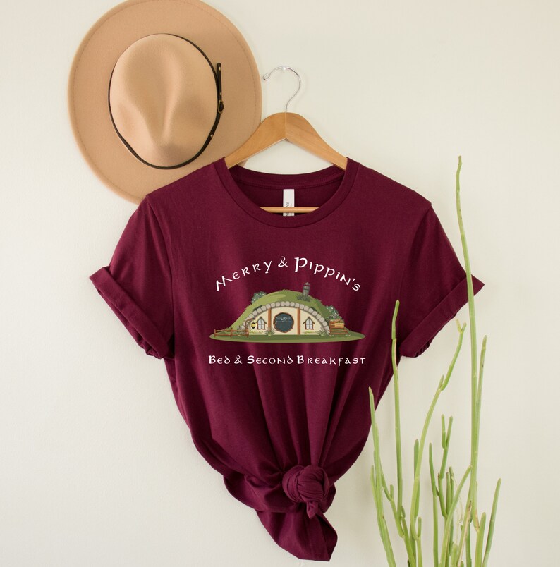 May include: A maroon t-shirt with a white graphic of a hobbit hole with the text "Merry & Pippin's Bed & Second Breakfast".