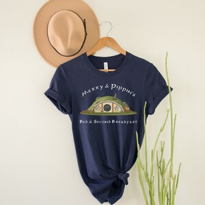 May include: A navy blue t-shirt with a white graphic of a hobbit hole with the text "Merry & Pippin's Bed & Second Breakfast".