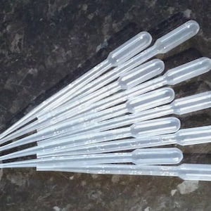Puede incluir: Un conjunto de pipetas de plástico transparente, cada una con una parte superior bulbosa y un cuerpo delgado y graduado. Las pipetas están dispuestas en forma de abanico, lo que sugiere un entorno de laboratorio o científico.