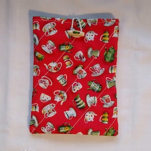 May include: Red quilted fabric pouch with a white button closure. The pouch is decorated with a repeating pattern of teacups and teapots.