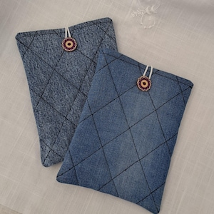 May include: Two denim-textured pouches with a quilted diamond pattern and dark stitching. Each pouch has a decorative wooden button with a floral design and a white string closure. The pouches are a medium blue color.