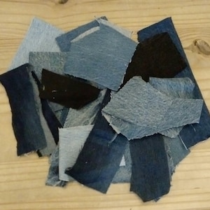 May include: A pile of denim fabric offcuts in shades of blue and black. The pieces are of various shapes and sizes, showing different textures and colour variations, indicating different washes and wear.