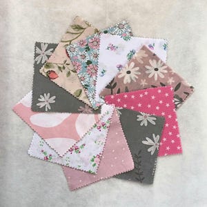 Puede incluir: Una colección de cuadrados de tela variados dispuestos en un patrón circular. Los cuadrados presentan patrones florales y geométricos en tonos de rosa, gris y blanco. Algunos cuadrados tienen diseños de margaritas y estrellas.