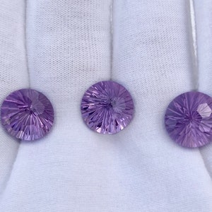 Może przedstawiać: Trzy okrągłe, fasetowane kamienie szlachetne ametystu w odcieniach fioletu, prezentowane na białym tle.