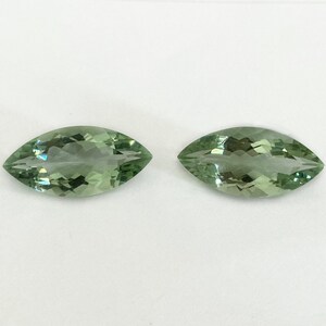 May include: Two marquise-shaped green gemstones, likely peridot or green amethyst, on a white background.