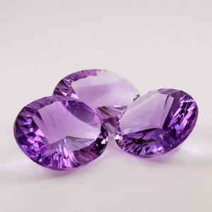 May include: Three faceted amethyst gemstones, cut in a round shape, with a purple hue. The gemstones are arranged in a cluster on a white background.