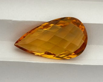 May include: A teardrop-shaped, faceted, orange gemstone. The gemstone is cut to a high polish and has a bright, clear color.