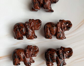 May include: Five small, carved stone elephant figurines. The elephants are a deep reddish-brown color with black veining. Each elephant has detailed features, including a trunk, ears, and tusks. The figurines are arranged on a white surface.