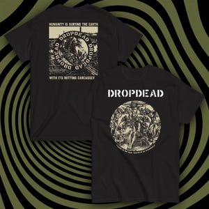 Puede incluir: Dos camisetas negras con diseños gráficos. Una camiseta tiene el texto "DROPDEAD" encima de una ilustración circular. La otra muestra "DROPDEAD" y un gráfico de la tierra con el texto: "HUMANITY IS BURYING THE EARTH WITH ITS ROTTING CARCASSES."