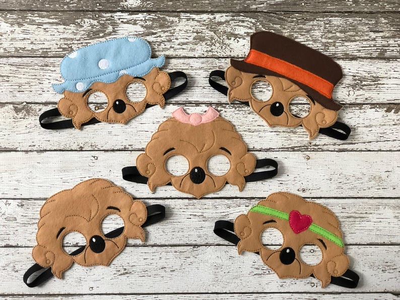 Five different felt bear masks with various hats and accessories are arranged on a white weathered wood surface.