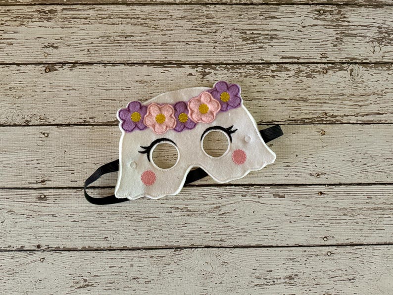 May include: White felt ghost mask with purple and pink flower embellishments around the eyes. The mask has black elastic straps.