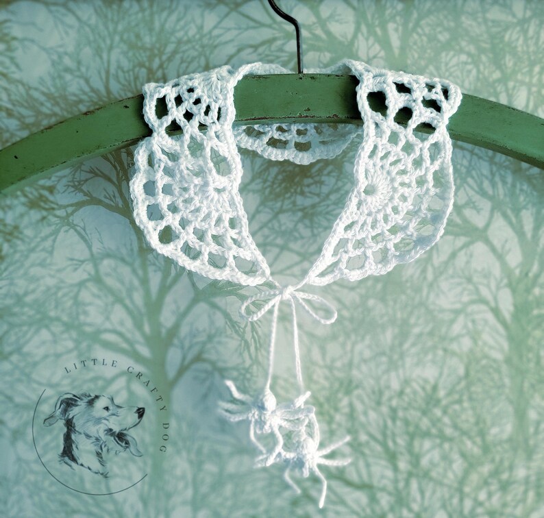 Puede incluir: Collar blanco de ganchillo en forma de telara&ntilde;a con una ara&ntilde;a de ganchillo blanca colgando de la parte inferior. El collar est&aacute; colgado de una percha verde sobre un fondo blanco.
