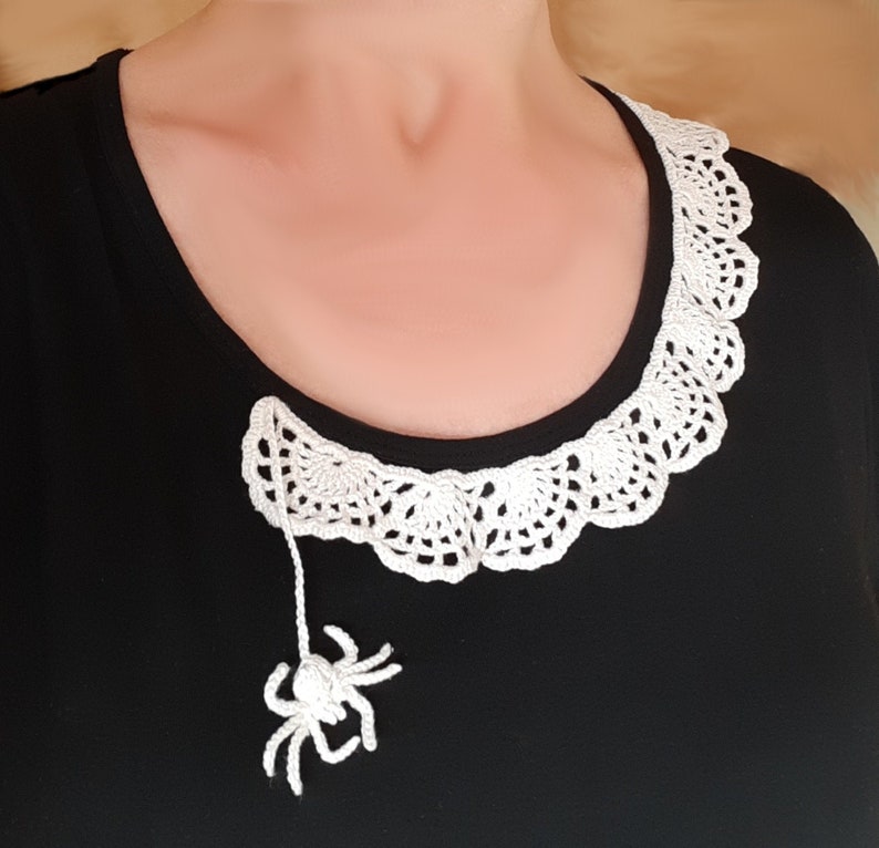 Puede incluir: Una camisa negra con un cuello de ganchillo blanco y una ara&ntilde;a de ganchillo blanco colgando del cuello.
