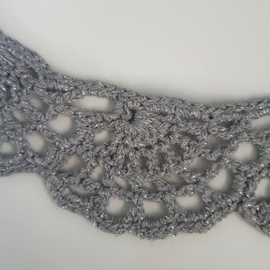 Puede incluir: Un collar de crochet plateado con un dise&ntilde;o delicado y de encaje. El collar est&aacute; hecho de un hilo brillante y tiene un borde festoneado.