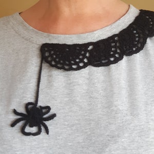 Puede incluir: Una camiseta gris con un dise&ntilde;o de telara&ntilde;a de ganchillo negro alrededor del escote. Una ara&ntilde;a de ganchillo negro cuelga de la telara&ntilde;a.