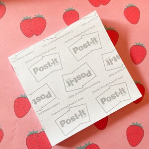 May include: A white Post-it Note pad with the text "Custom Printed Post-it Note" and the Post-it brand logo. The pad is on a pink background with a pattern of red strawberries.