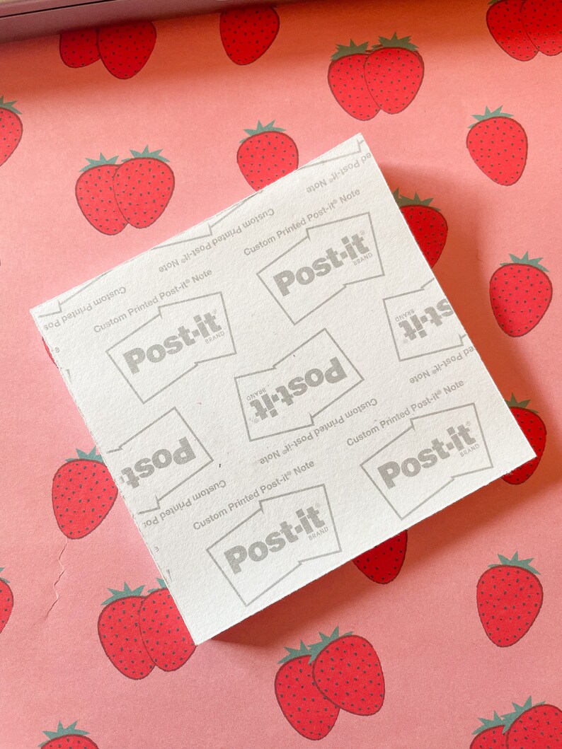 May include: A white Post-it Note pad with the text "Custom Printed Post-it Note" and the Post-it brand logo. The pad is on a pink background with a pattern of red strawberries.