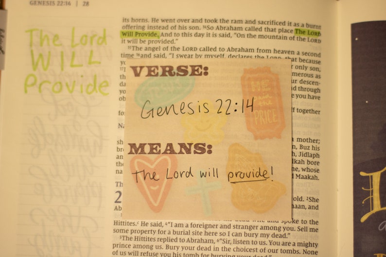 May include: A close-up of a page from a Bible with the text "The Lord Will Provide" highlighted in green. The verse "Genesis 22:14" is written in black marker on a yellow background with a heart shape and the words "The Lord will provide!" written in black marker.