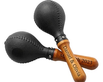 May include: A pair of black maracas with wooden handles. The handles are engraved with the text "Daniel & Olivia" and "March 2023".