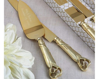 May include: Gold wedding cake knife set with a heart-shaped handle. The knife is engraved with the names "Bill & Jackie" and the date "November 19, 2020".
