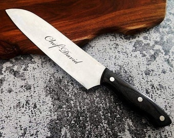 Puede incluir: Un cuchillo de chef plateado con mango negro y la inscripción "Chef David" en la hoja. El cuchillo está apoyado en una tabla de cortar de madera.