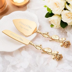 May include: Gold-tone wedding cake knife and server set with rose-shaped handles. The handles are engraved with the text "Married & Date" and the date "May 15th, 2025".