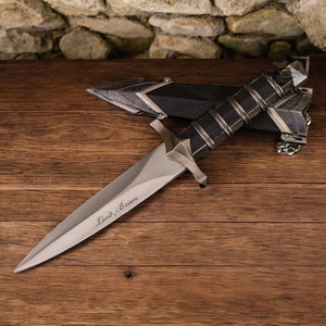 Könnte beinhalten: Ein silbernes Dolch mit schwarzem Griff und einer Lederscheide. Die Klinge ist mit den Worten "Lord Brian" graviert.