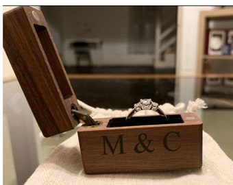 May include: A wooden ring box with a hinged lid, engraved with "M & C". A silver ring with three diamonds is inside the box.