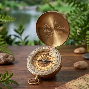 May include: A brass pocket compass with a hinged lid featuring an engraved message that reads: Aidan, I hope you always follow your heart, Love Mom. The compass has a circular face with cardinal directions and a central needle on a white background.