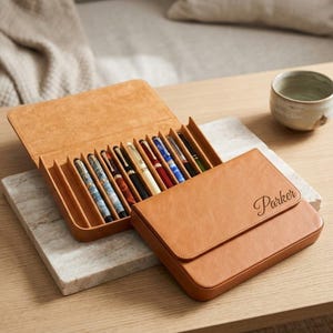 May include: A tan leather pen case with a flap closure featuring the name Parker embossed in script. The open case reveals eight individual slots, each containing a fountain pen with various barrel colours including blue, red, and black.