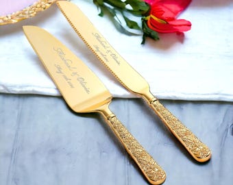 May include: A gold-colored cake knife and server set. The knife has a serrated blade, and both pieces have ornate floral-patterned handles. The set is engraved with the names "Michael & Olivia" and the date "Stay with us 2024".