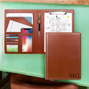 May include: A brown leather portfolio with a built-in notepad, pen holder, and slots for cards and a phone. The portfolio has a calendar page with the year 2019 and the month of May. The portfolio has the initials "MG" embossed on the front.