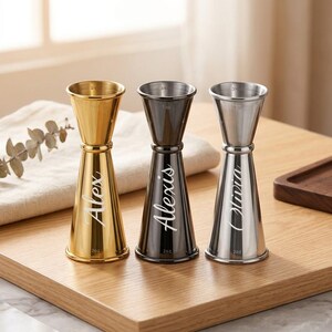 May include: Three double-sided metal jiggers in gold, gunmetal, and silver finishes. Each jigger features a tapered hourglass shape with engraved names: Alex on the gold, Alexis on the gunmetal, and Olivia on the silver. Each has 3/4 oz and 2 oz markings.