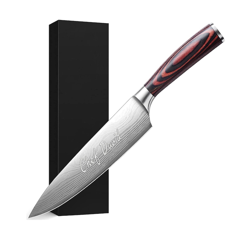 May include: A stainless steel chef's knife with a patterned blade and a wooden handle with red and brown tones. The text "Chef David" is etched on the blade. A black box is in the background.
