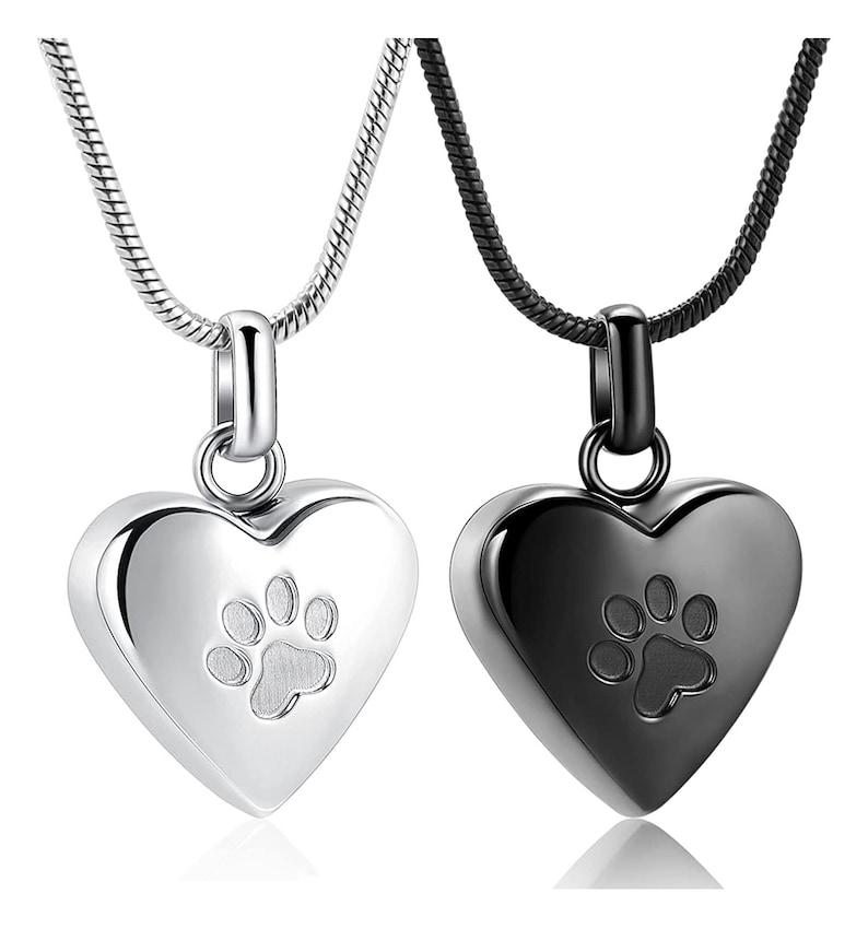 May include: Two heart-shaped cremation pendants with paw print designs. One pendant is silver and the other is black. Both pendants are on silver and black chains.