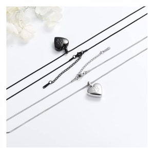 May include: Two silver heart-shaped cremation necklaces with a paw print design. One necklace has a black chain and the other has a silver chain.