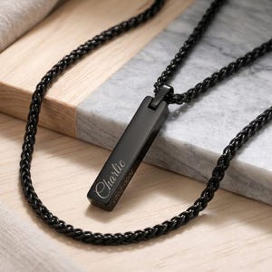 May include: A black metal bar pendant necklace featuring a wheat chain. The rectangular pendant is engraved with the name Charlie in a cursive script font, followed by the years 2000-2025 in a clean, sans-serif typeface on the side edge.