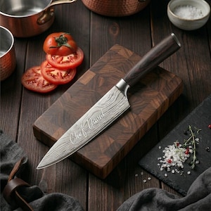Puede incluir: Un cuchillo de chef con una hoja estampada y un mango de madera oscura descansa sobre una tabla de cortar de madera. La hoja est&aacute; grabada con "Chef David". Tambi&eacute;n se ven tomates en rodajas y un peque&ntilde;o cuenco de sal.