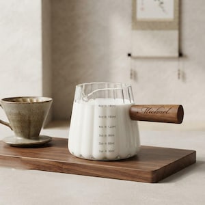 May include: A clear glass pitcher with a fluted design and a wooden handle engraved with the name Michael. The pitcher features printed measurement markings from 1oz to 6oz and 30ml to 180ml, accompanied by a speckled ceramic coffee dripper.