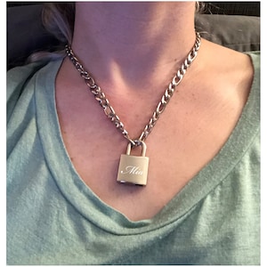 May include: A silver chain necklace with a silver padlock pendant. The padlock has the name "Mia" engraved on it.