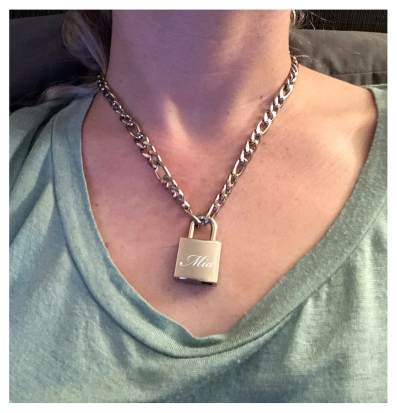 May include: A silver chain necklace with a silver padlock pendant. The padlock has the name "Mia" engraved on it.