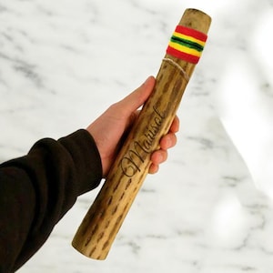 May include: A wooden percussion instrument called a "Marisoul" with a red, yellow, and green striped band around the top. The instrument is made of natural wood and has a rough texture.