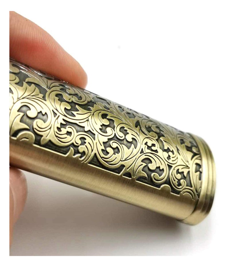 Puede incluir: Un encendedor de color dorado con un intrincado dise&ntilde;o floral grabado en la superficie. El encendedor tiene una forma redondeada y un acabado liso.