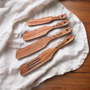 May include: Set of four wooden kitchen spatulas with the text "The Smiths" engraved on each. The spatulas are different sizes and one has a slotted design.