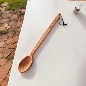 May include: A long wooden spoon with a black string attached to the handle. The spoon is engraved with the text "Olivia & David".