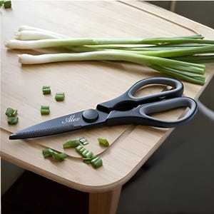 May include: Black kitchen shears with a grey handle and a personalized inscription that reads "Alex". The shears are on a wooden cutting board with chopped green onions.