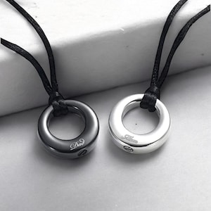 May include: Two black cord necklaces with silver and black round pendants. The silver pendant has the word "Mom" engraved on it and the black pendant has the word "Dad" engraved on it.