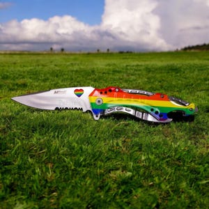 May include: A rainbow-colored pocket knife with a silver blade and a heart-shaped design. The knife is engraved with the name "Patrick".