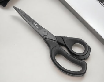 May include: A pair of black, metal scissors with a black plastic handle. The scissors have a silver blade and the word "Blake" is printed on the handle.