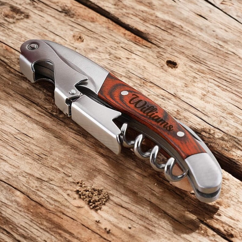 May include: A silver and wood wine opener with a corkscrew and bottle opener. The handle is engraved with the name "Williams".